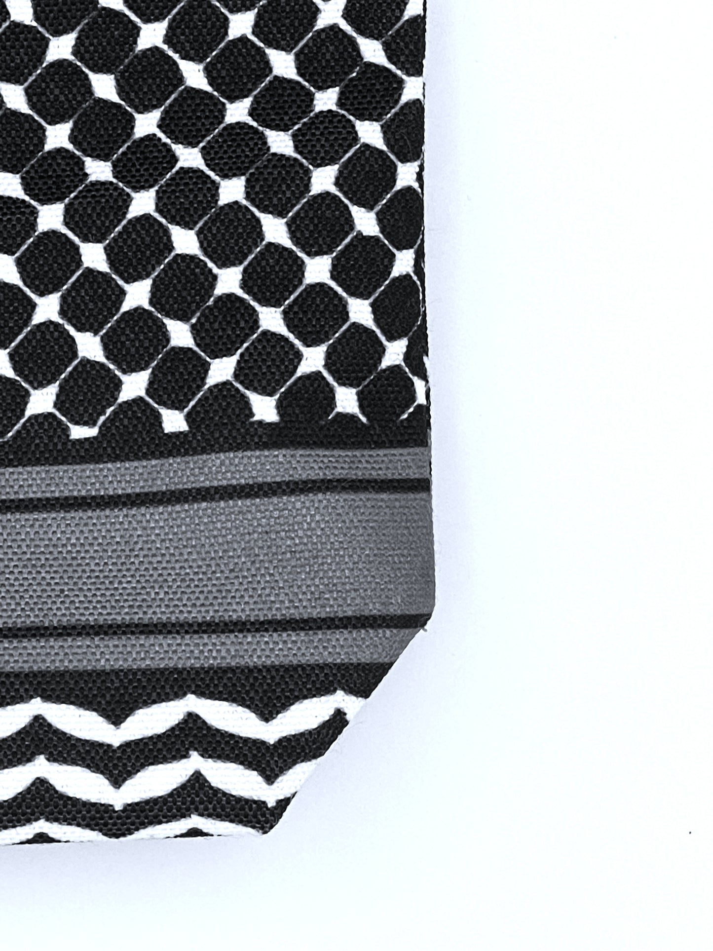 Macro shot of corner of black makeup bag against white background showcasing keffiyeh pattern design.