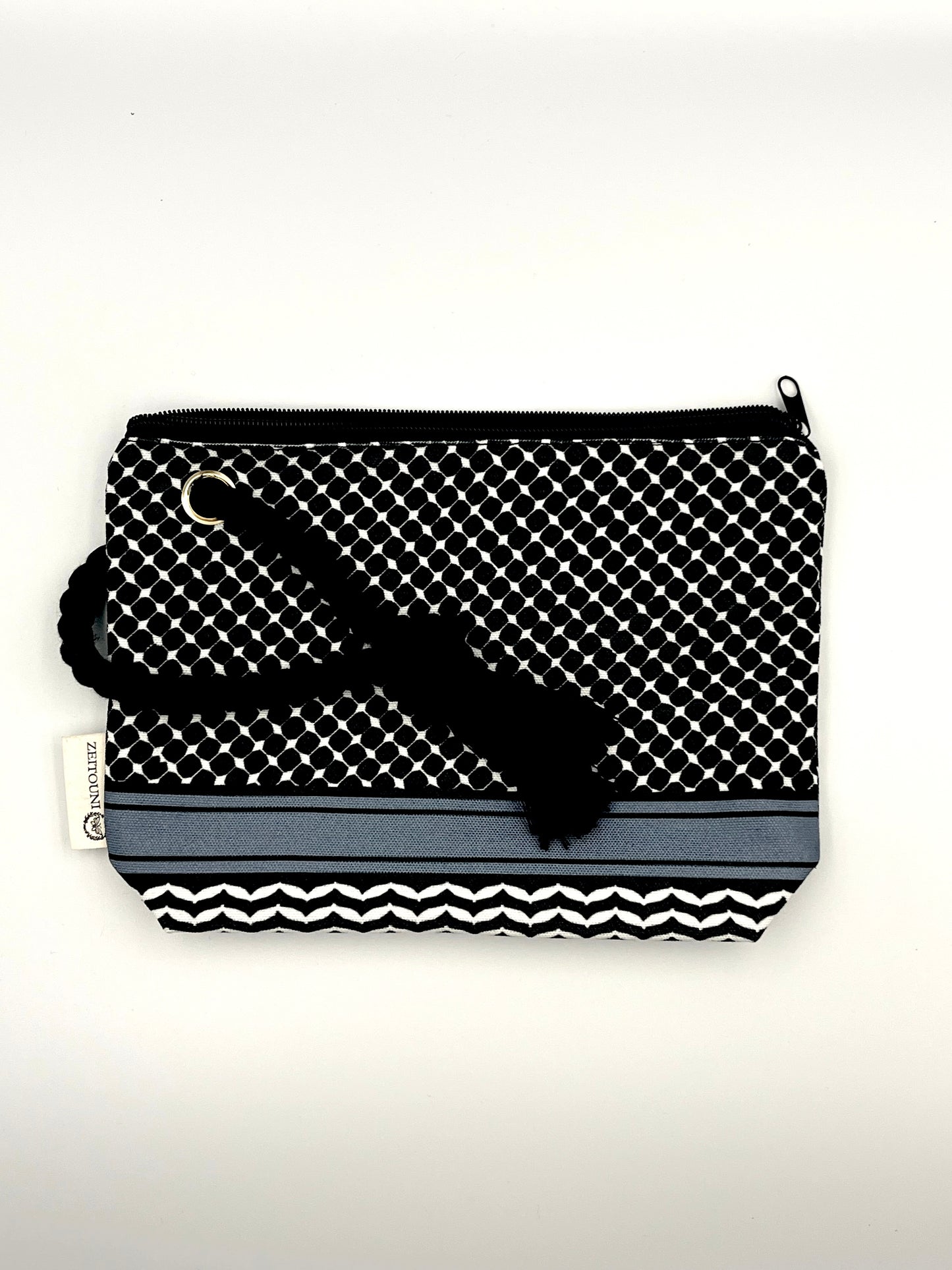Black makeup bag with black rope against a white background with rope laid diagonally across the bag. Bag is patterned with a keffiyeh design and a ZEITOUNI logo tag. 