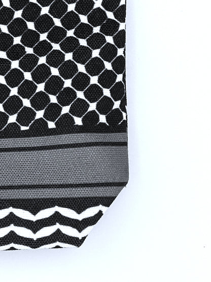 Macro shot of corner of black makeup bag against white background showcasing keffiyeh pattern design. 