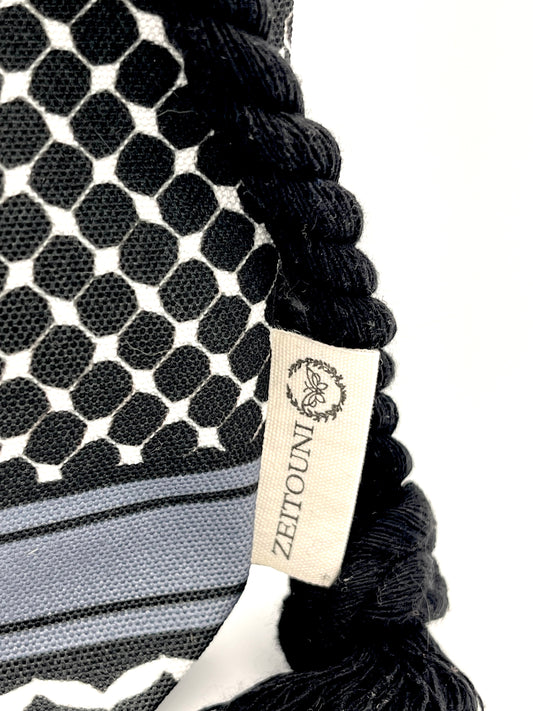 Macro shot of black makeup bag with black rope showcasing keffiyeh design and ZEITOUNI logo tag against a white background. 