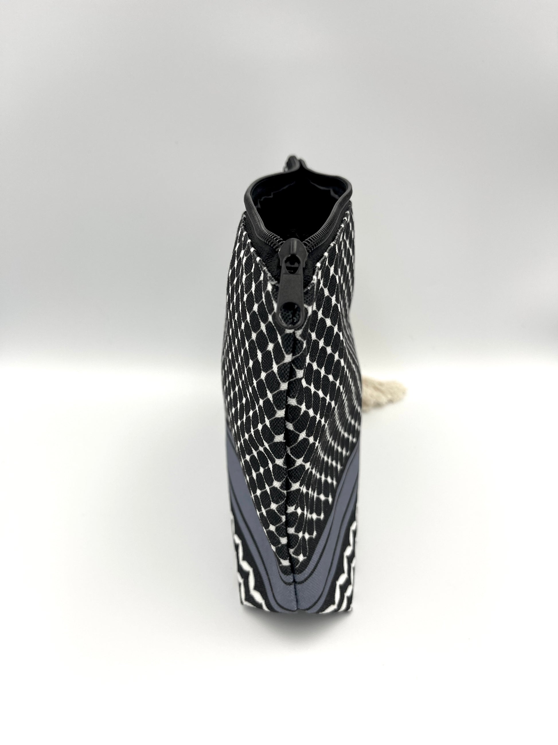 Side image of black makeup bag with beige rope against white background, showcasing zipper lip of the bag. Bag is designed with a black keffiyeh pattern. 