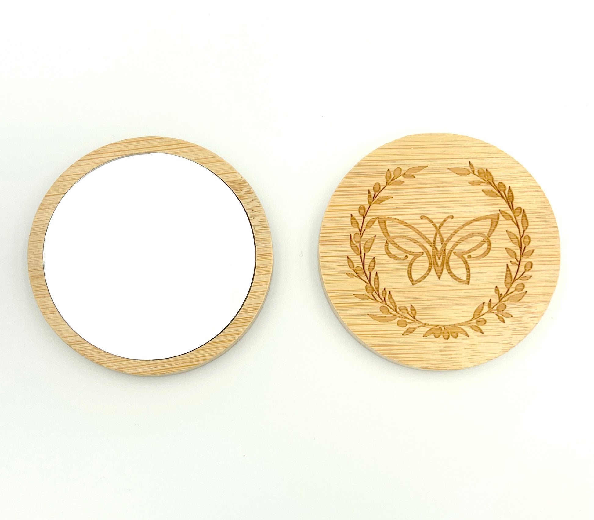 Bamboo mirror front and back facing on a white background. Back is decorated with logo of butterfly surrounded by olive wreath.