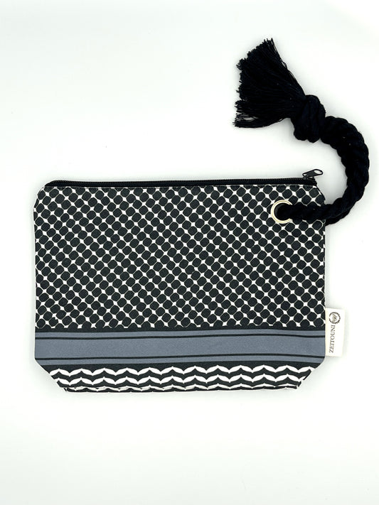Black makeup bag with black rope handle against a white backround. Bag is patterned with a black keffiyeh pattern and a ZEITOUNI logo tag.