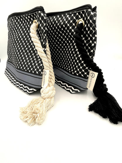 Angle shot of two black makeup bags against a white background. Left bag has beige rope, right bag has black rope. Both bags are designed with black keffiyeh pattern and ZEITOUNI logo tag. 